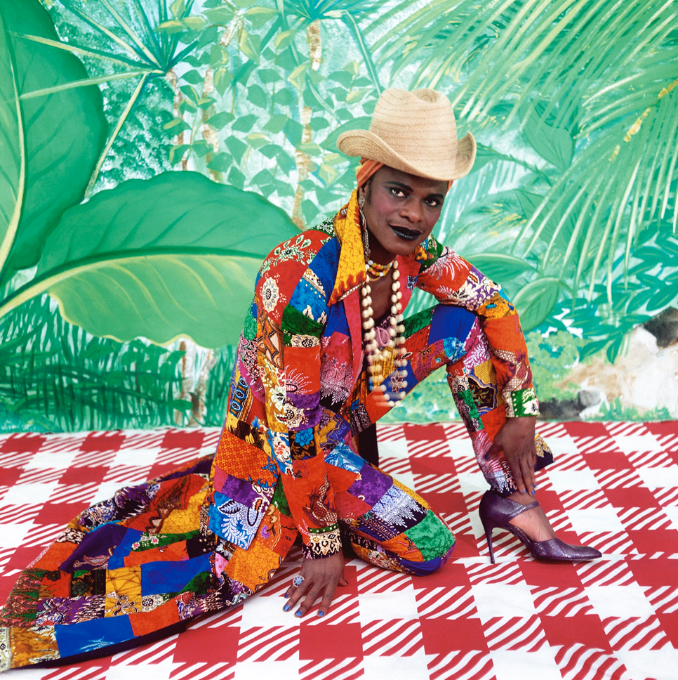 black man, sitting, wearing a cowboy-hat and colourful woman's clothes